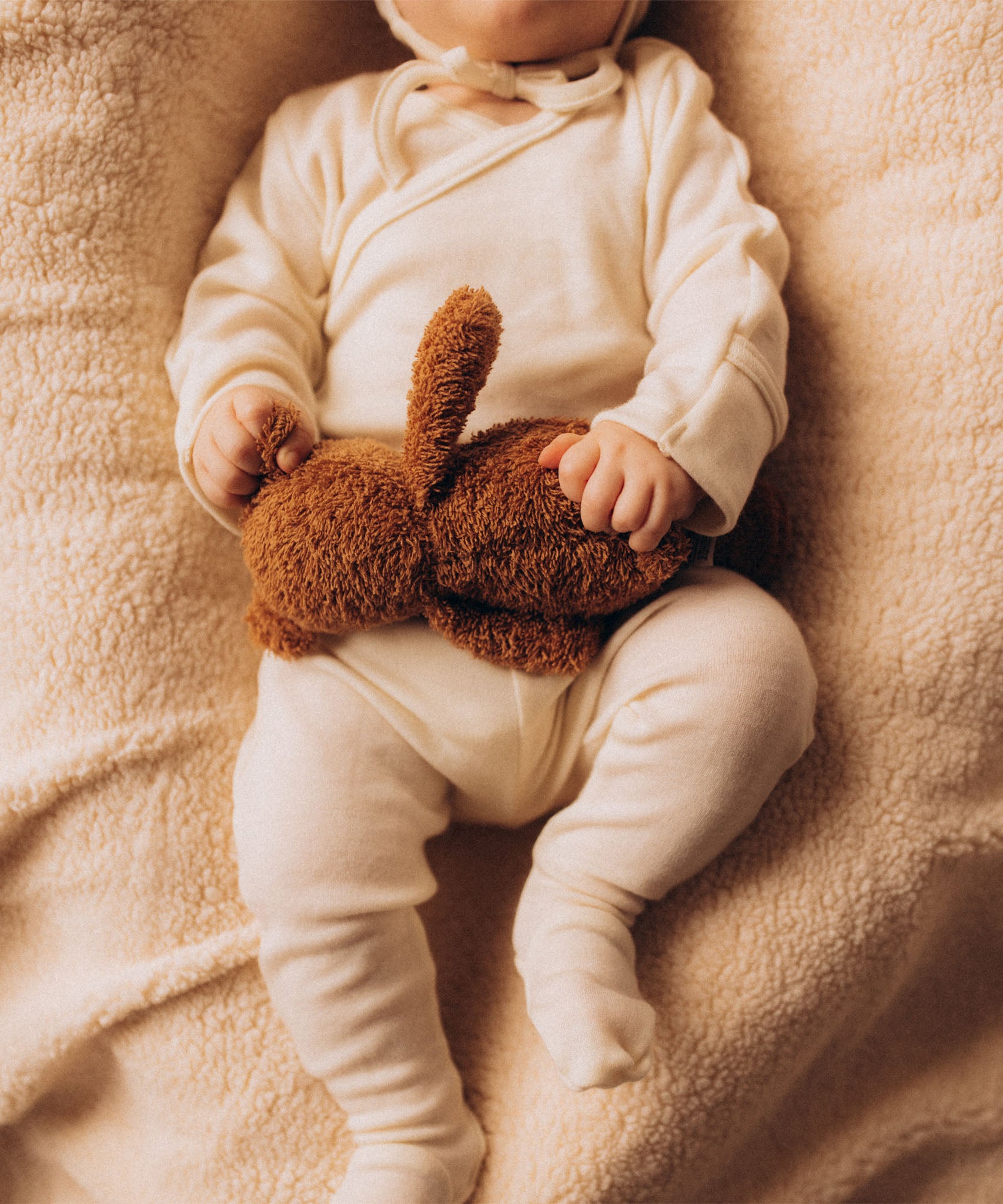 A close up of a baby holding onto the A small Wooly Organic soft teddy bear in brown available at Babipur. 