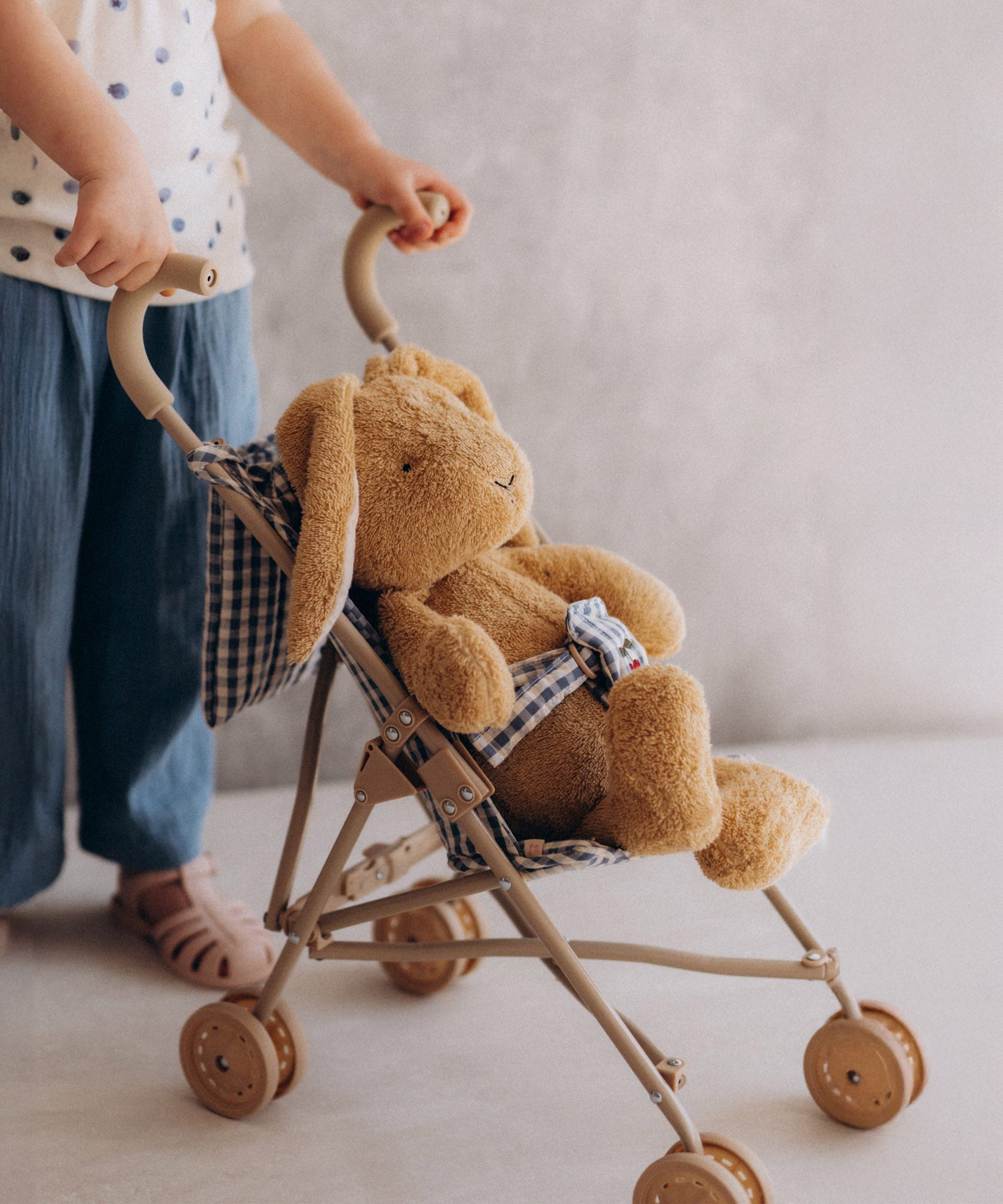A toddler pushing the Wooly Organic soft cotton bunny rabbit toy in a toy pram. Bunny rabbit available at Babipur. 