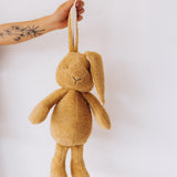 A adult holding the Wooly Organic soft cotton bunny rabbit toy in light brown colour by the floppy ears. Bunny rabbit available at Babipur. 