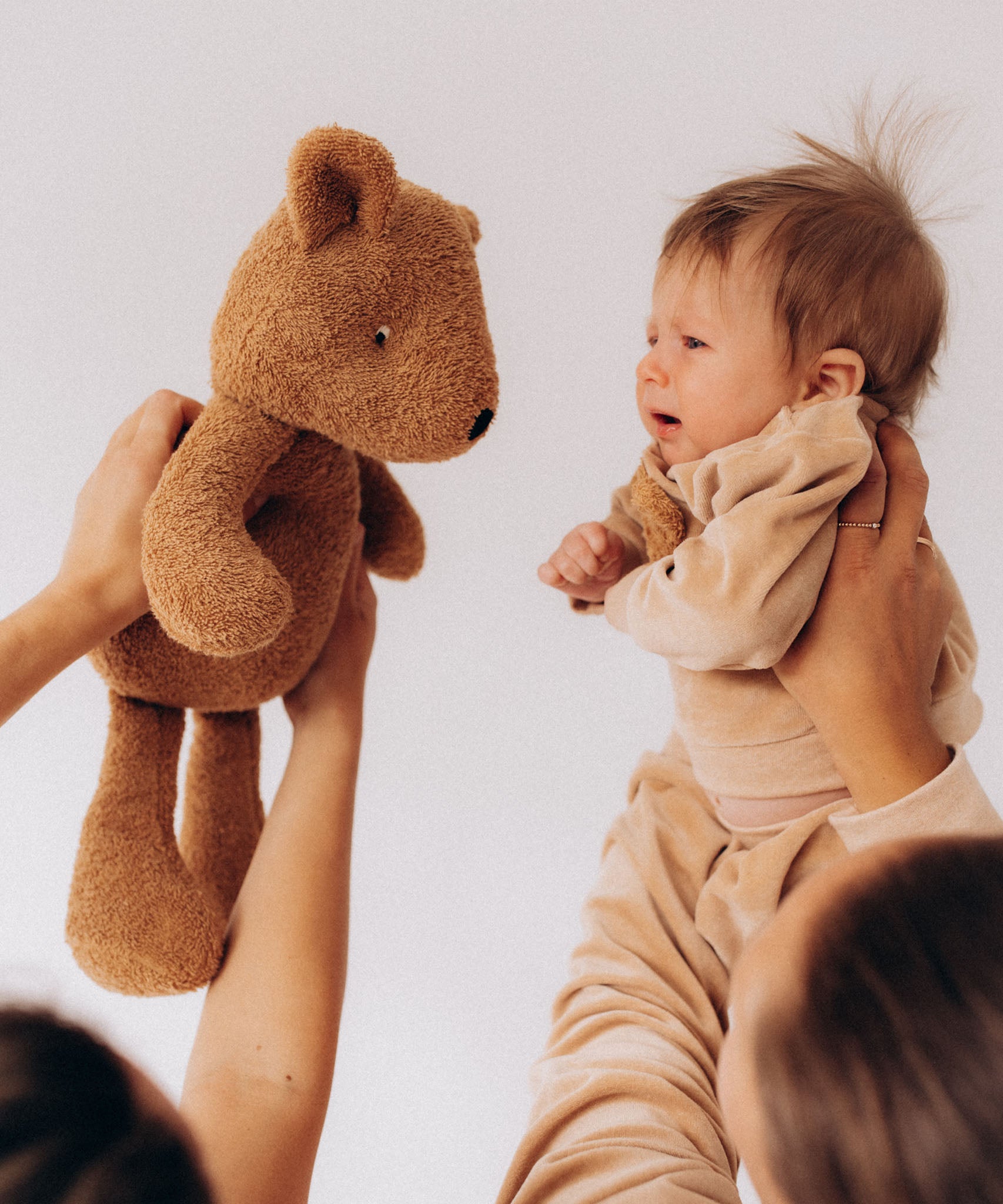 A baby being held next to a Wooly Organic soft teddy bear in caramel brown available at Babipur.