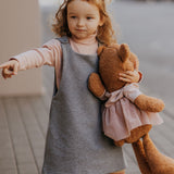 A child walking down a street holding the Wooly Organic soft teddy bear in caramel brown with a pink tutu available at Babipur. 