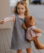 A child walking down a street holding the Wooly Organic soft teddy bear in caramel brown with a pink tutu available at Babipur. 