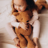 A small child hugging the Wooly Organic soft teddy bear in caramel brown available at Babipur.