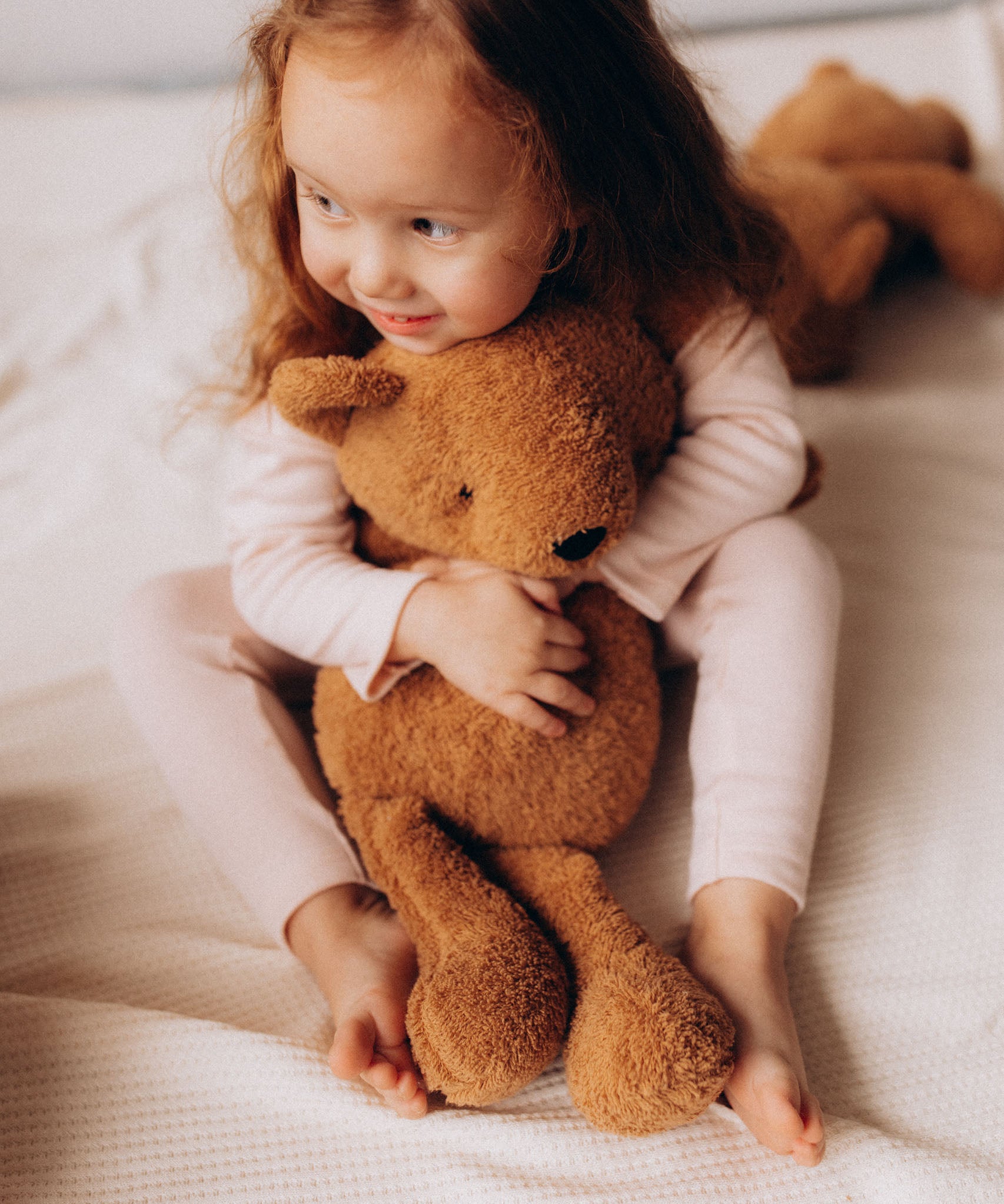 A small child hugging the Wooly Organic soft teddy bear in caramel brown available at Babipur.