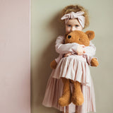 A child hugging the Wooly Organic soft teddy bear in caramel brown with a pink tutu available at Babipur. 