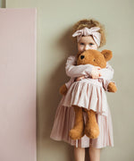A child hugging the Wooly Organic soft teddy bear in caramel brown with a pink tutu available at Babipur. 