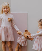 2 children holding the Wooly Organic soft teddy bear in caramel brown with a pink tutu by the hand. Teddy bear available at Babipur. 