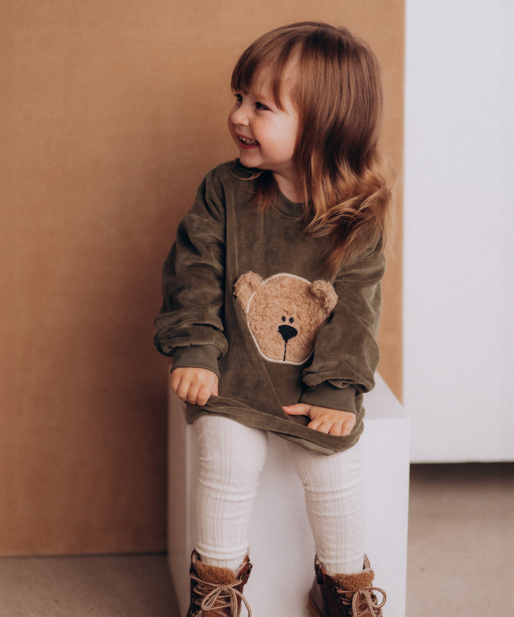 A girl wearing the Wooly Organic embroidered GOTS organic cotton velour sweater in tea leaf /savannah available at Babipur. 