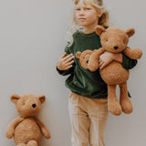A child wearing the Wooly Organic tea leaf velour embroidered sweater and holding the soft teddy bear in caramel, both available at Babipur. 