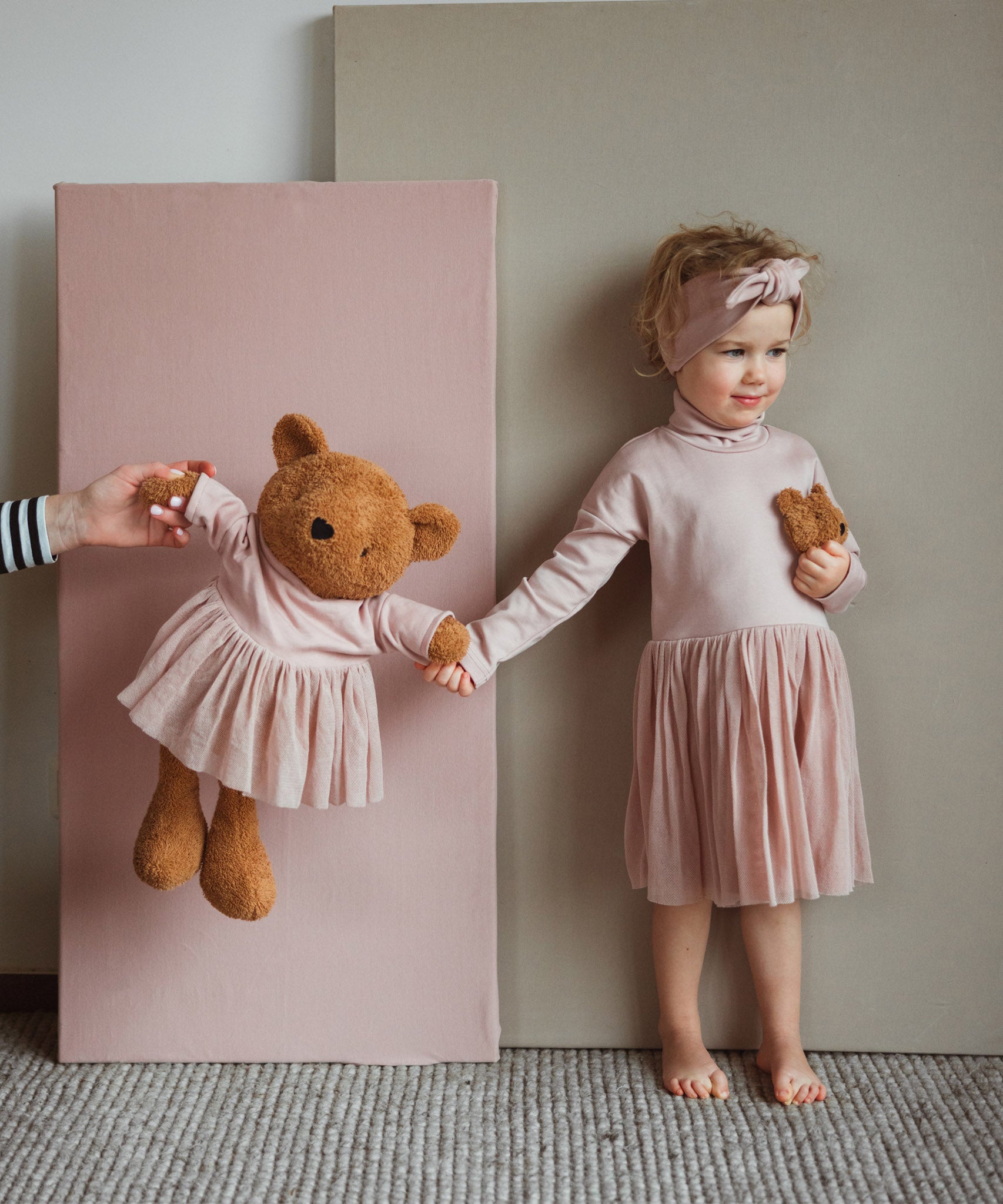 A child standing next to the Wooly Organic soft teddy bear in caramel brown with a pink tutu and holding by the hand. Teddy bear available at Babipur. 