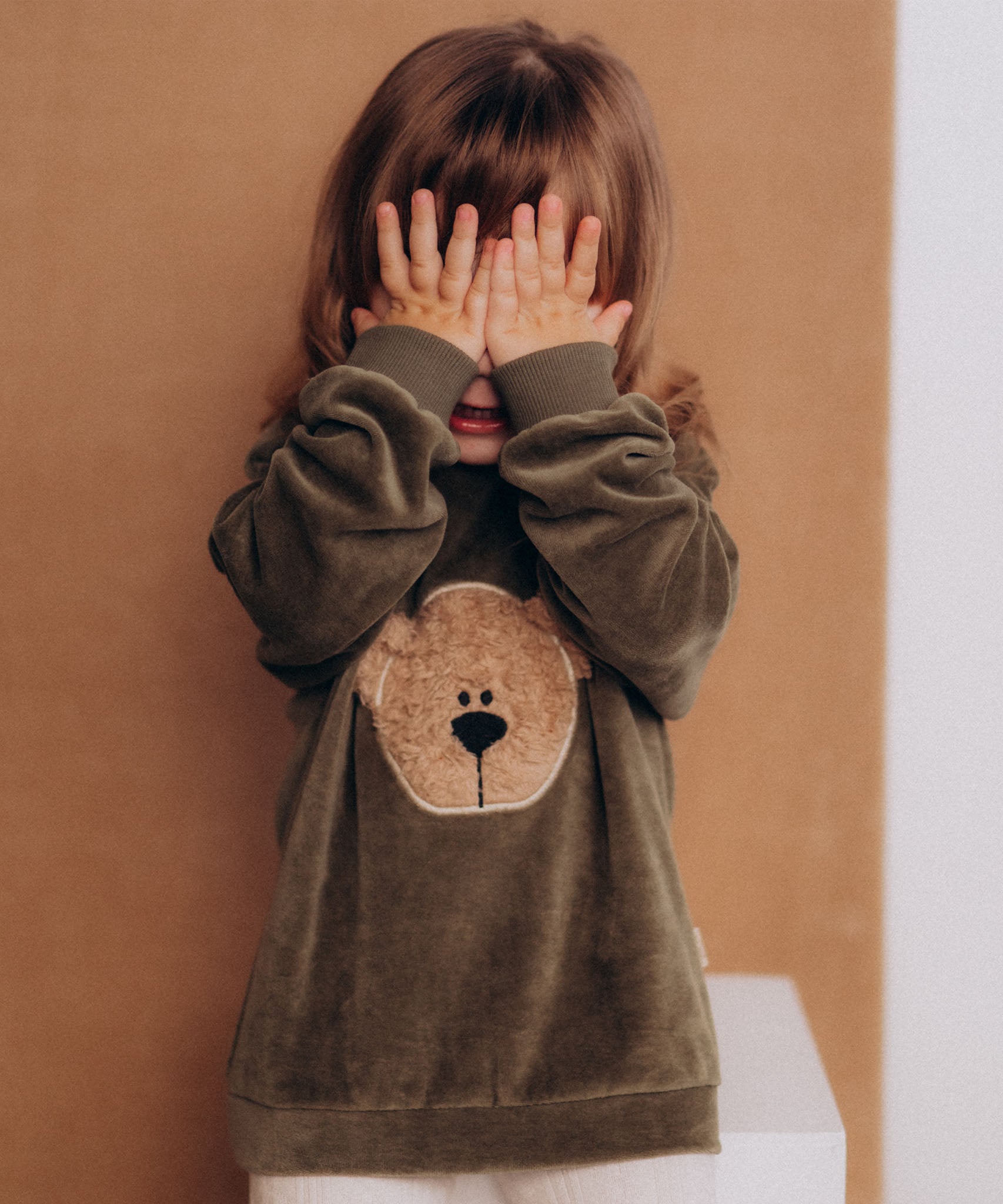 A child playing and wearing the Wooly Organic embroidered GOTS organic cotton velour sweater in tea leaf /savannah available at Babipur. 