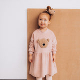 A child wearing the Wooly Organic embroidered velour dress in pale blush pink /savannah available at Babipur. A soft GOTS organic cotton velour sweater in light pink with a cute fluffy cream teddy bear on the front 