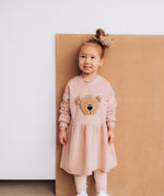A child wearing the Wooly Organic embroidered velour dress in pale blush pink /savannah available at Babipur. A soft GOTS organic cotton velour sweater in light pink with a cute fluffy cream teddy bear on the front 