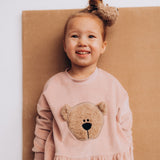 A close up of a child wearing the Wooly Organic embroidered velour dress in pale blush pink /savannah available at Babipur showing the fluffy teddy bear embroidery detail