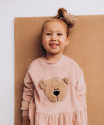 A close up of a child wearing the Wooly Organic embroidered velour dress in pale blush pink /savannah available at Babipur showing the fluffy teddy bear embroidery detail