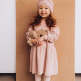 A child wearing the Wooly Organic embroidered teddy bear velour dress in pale blush pink /savannah available at Babipur.