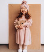 A child wearing the Wooly Organic embroidered teddy bear velour dress in pale blush pink /savannah available at Babipur.