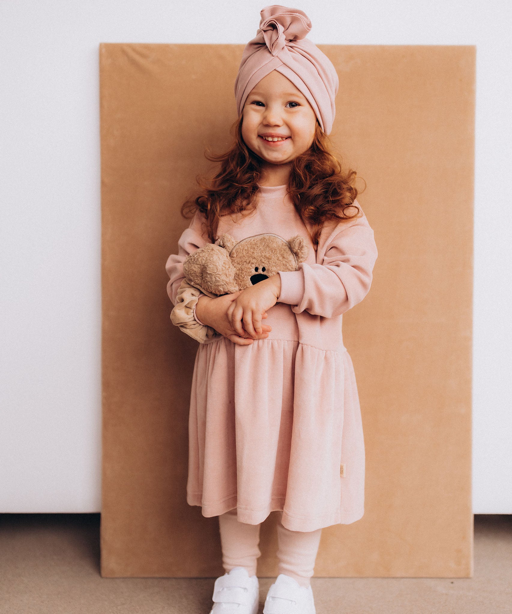 A child wearing the Wooly Organic embroidered teddy bear velour dress in pale blush pink /savannah available at Babipur.