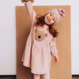 A child modelling the Wooly Organic embroidered velour dress in pale blush pink /savannah available at Babipur showing the fluffy teddy bear embroidery detail on GOTS organic cotton fabric