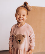 A child wearing the Wooly Organic velour scrunchy in cream with a fluffy teddy on their head. Scrunchy available at Babipur. 