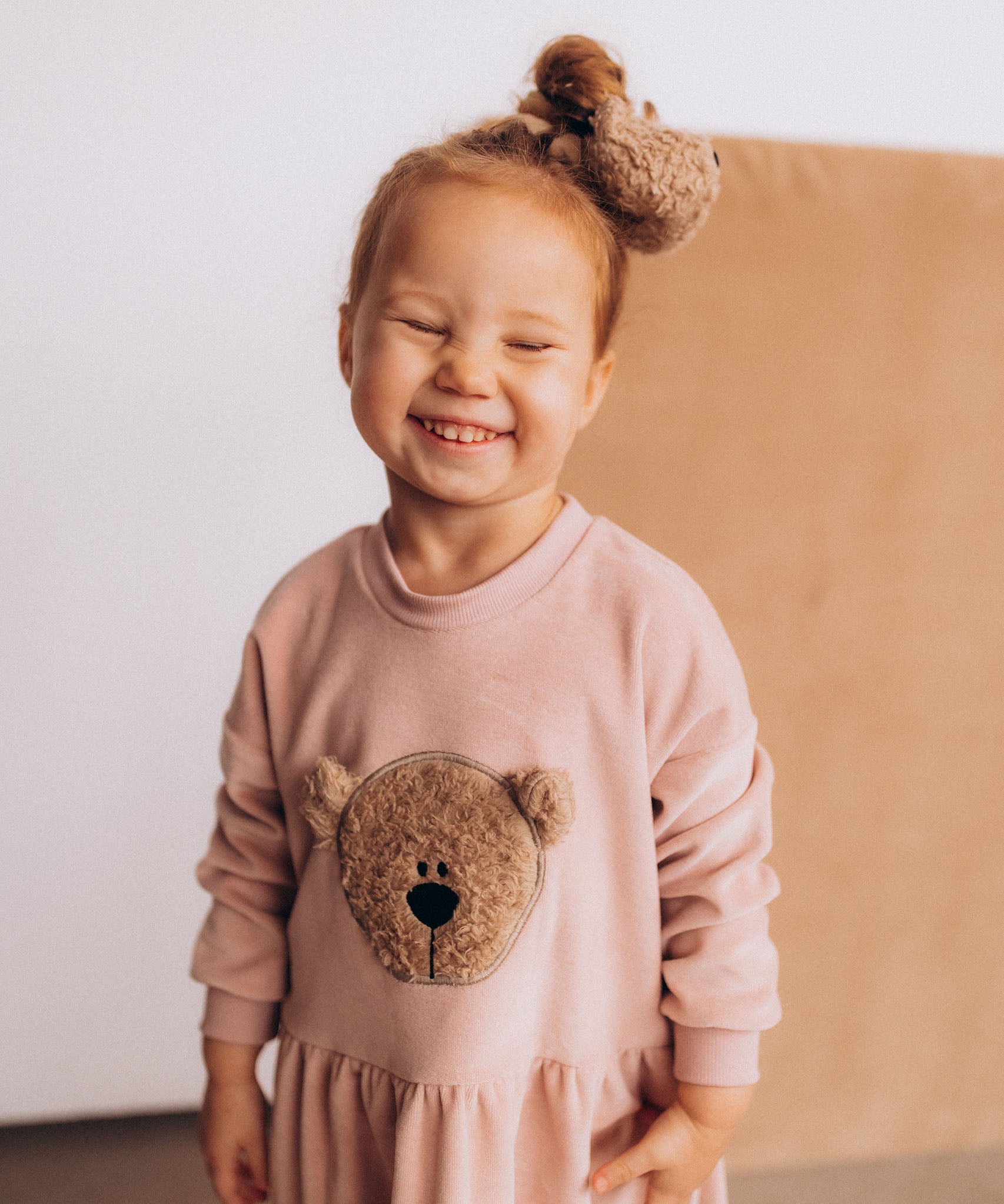 A child wearing the Wooly Organic velour scrunchy in cream with a fluffy teddy on their head. Scrunchy available at Babipur. 