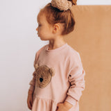 A child wearing the Wooly Organic velour scrunchy in cream with a fluffy teddy attached in matching colour available at Babipur. 
