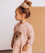 A child wearing the Wooly Organic velour scrunchy in cream with a fluffy teddy attached in matching colour available at Babipur. 