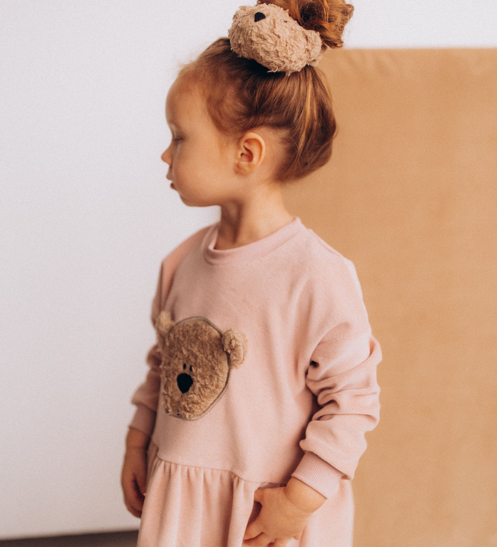 A child wearing the Wooly Organic velour scrunchy in cream with a fluffy teddy attached in matching colour available at Babipur. 