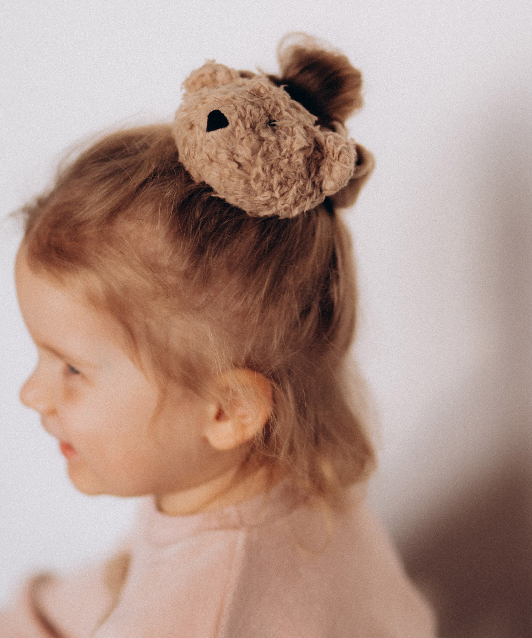 A close up of a child wearing the Wooly Organic velour scrunchy available at Babipur showing the cute fluffy teddy bear detail