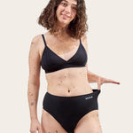 An adult wearing the WUKA Stretch Cotton Midi Brief Period Pants Black - Heavy Flow shown from the front on a cream background