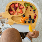 Baby sitting in a high chair choosing fruit from a bamboo elephant weaning plate.