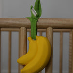 The Ana Banana Pacifier Holder is attached to the side of a wooden cot, with the muslin cloth leaves.
