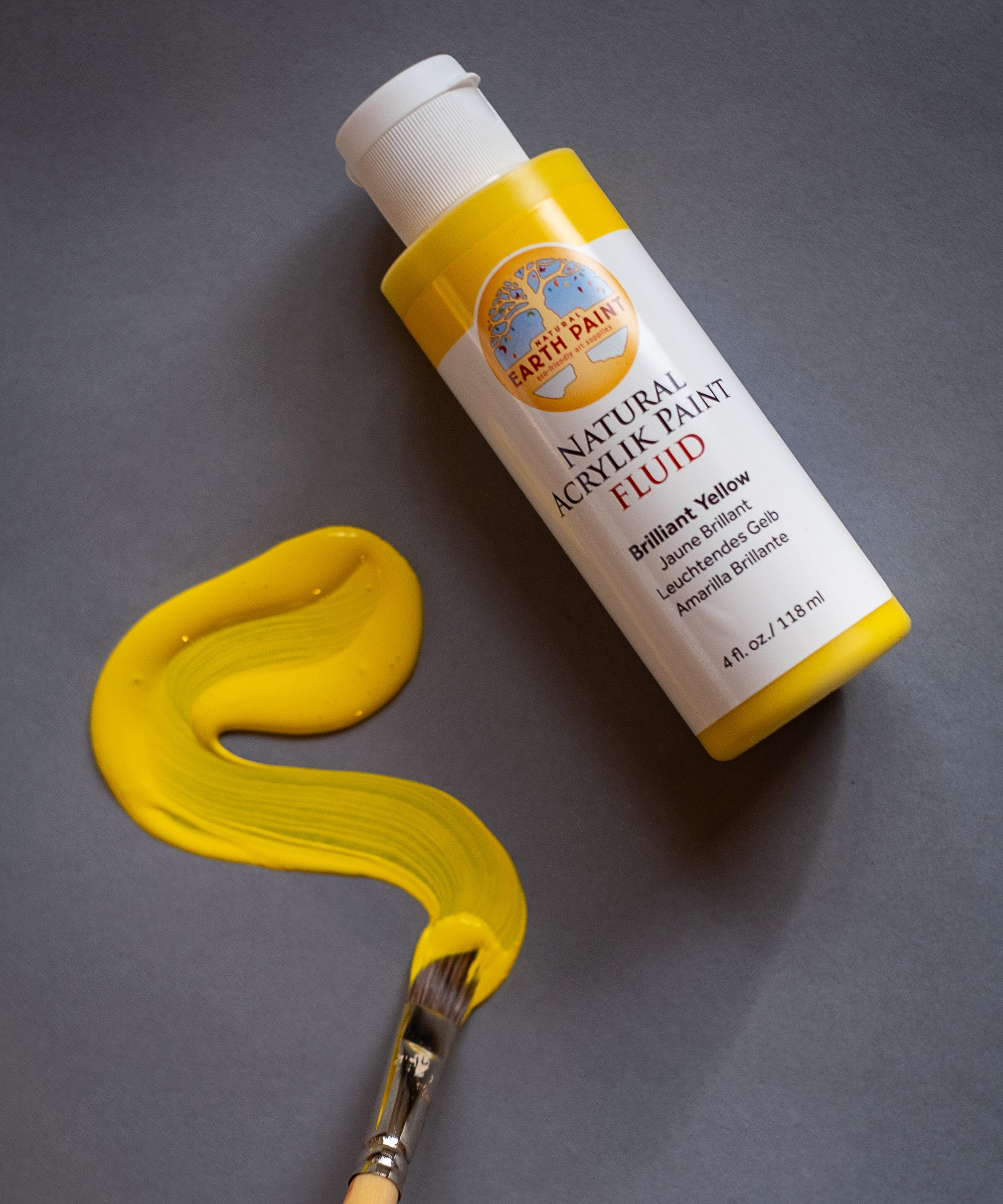 A Close up view of the Natural Earth Paint brilliant yellow acrylic paint with a brush 