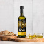 Zaytoun Organic Extra Virgin Olive Oil - 500ml stood on a wooden chopping board, next to a loaf of bread and glass ramekins filled with olive oil