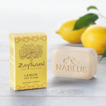Zaytoun Pure Olive Oil Soap - Lemon 100g, next to its box and stood in front of a pair of lemons