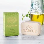 Zaytoun Pure Olive Oil Soap 100g, next to its box and stood in front of a glass jar of olive oil