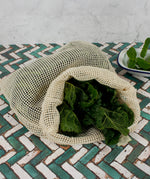 A Slice Of Green large mesh produce bag made from recycled cotton on a tiled surface showing a bunch of cabbage leave inside showing scale. 