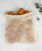 A Slice Of Green large mesh produce bag made from recycled cotton laid flat on a stone surface showing a bunch of potatoes inside showing scale.
