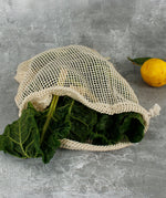 A open A Slice Of Green large mesh produce bag laid flat on a wooden surface showing a bunch of cabbage leaves inside the opened bag showing scale. 