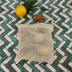 A Slice Of Green small mesh produce bag made from recycled cotton showing a bunch of food items inside next a lemon showing scale. 