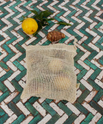 A Slice Of Green small mesh produce bag made from recycled cotton showing a bunch of food items inside next a lemon showing scale. 