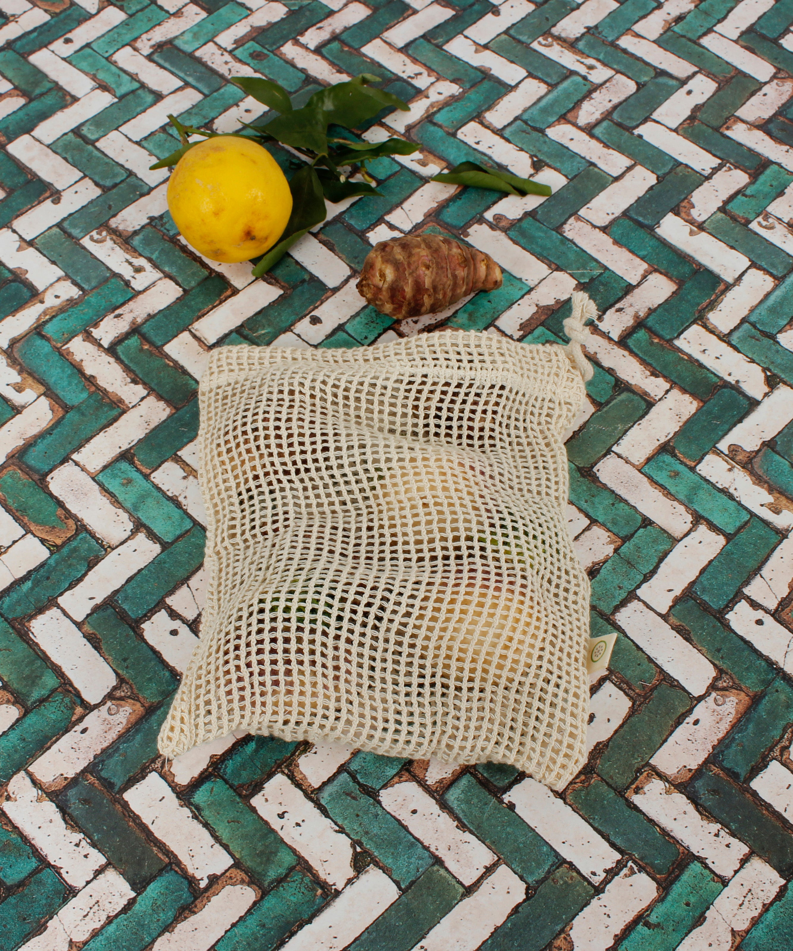 A Slice Of Green small mesh produce bag made from recycled cotton showing a bunch of food items inside next a lemon showing scale. 