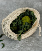 A Slice Of Green large mesh produce bag made from recycled cotton on a stone surface showing fresh produce inside the opened bag