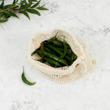 A open A Slice Of Green small mesh produce bag. A recycled cotton bag showing a bunch of green chilles inside  showing scale. 