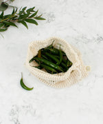 A open A Slice Of Green small mesh produce bag. A recycled cotton bag showing a bunch of green chilles inside  showing scale. 