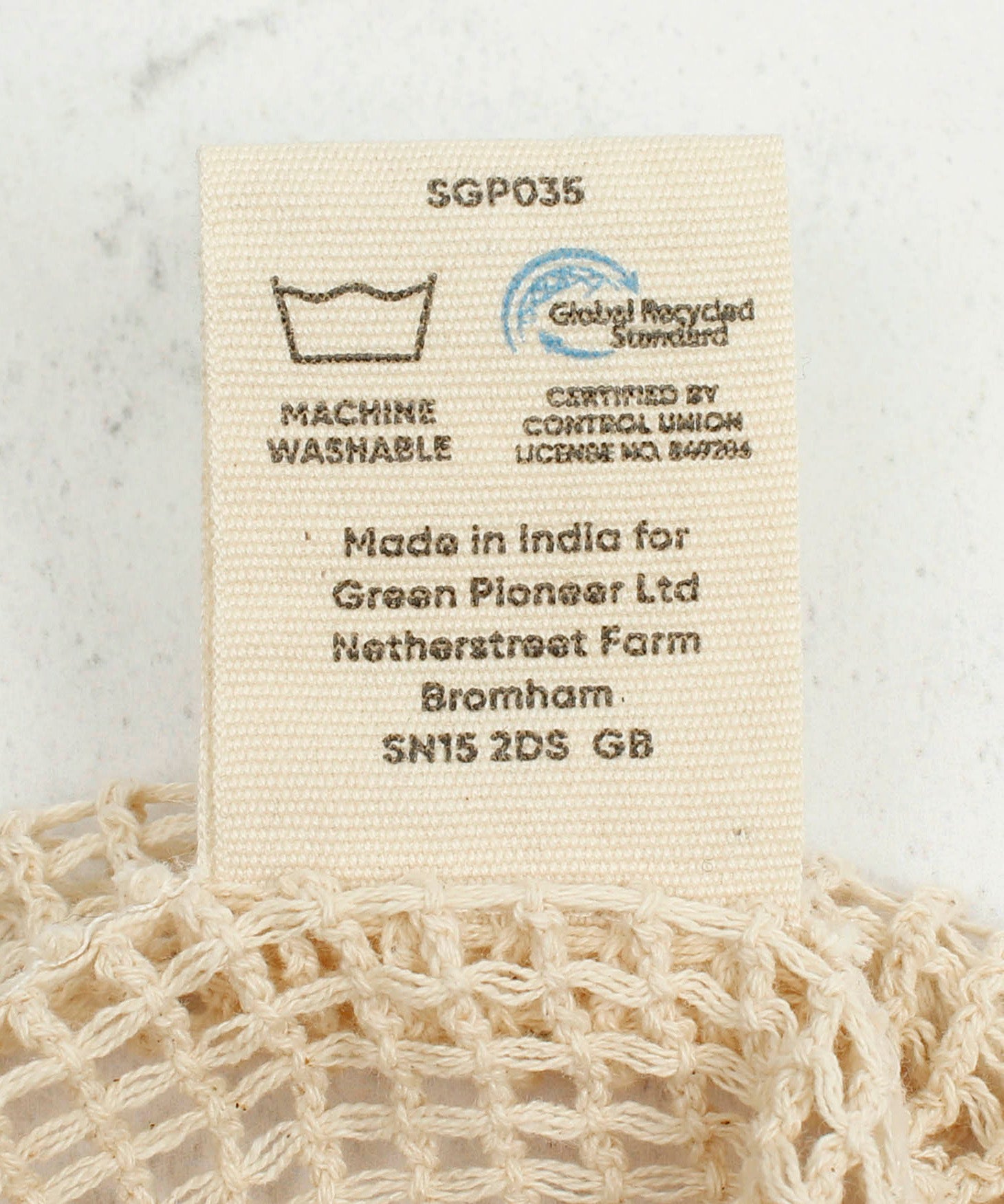 A close up view of the A Slice Of Green small mesh recycled cotton produce bag showing the certifications tag 
