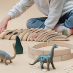 Close up of child playing with some dinosaur toys and a set of Abel mini wooden curved block toys on a beige background