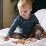 Young boy sat on a white bed playing with the Abel stacking wooden Golden Ratio toy blocks