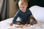 Young boy sat on a white bed playing with the Abel stacking wooden Golden Ratio toy blocks