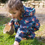 A child outside wearing the Frugi Children's Puddle Buster All In One - Tiger Time. The image also shows part of the hood